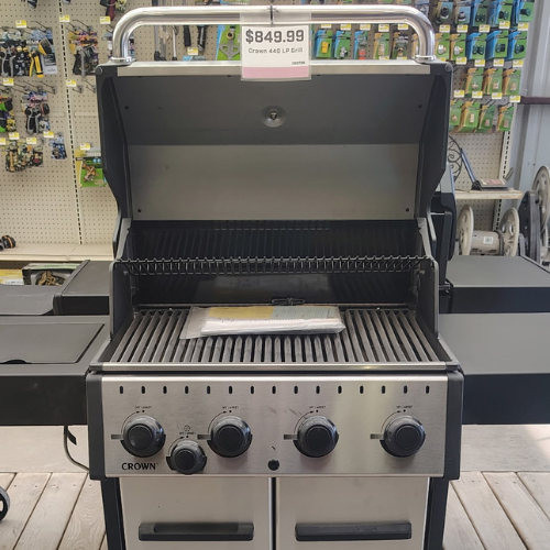 Open stainless steel Crown gas grill displayed in a store, priced at $849.99, with burners and warming rack visible; practical retail setting.
