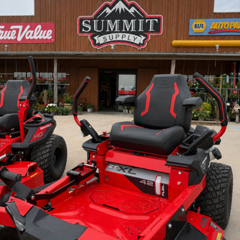 Two red zero-turn lawn mowers sit outside Summit Supply, with black seats and rugged tires; storefront signs and plants create a practical scene.