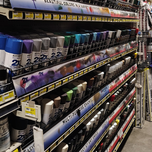 Retail store aisle stocked with rows of colorful spray paint cans, including Rust-Oleum and Easy spray brands, under bright product signs.