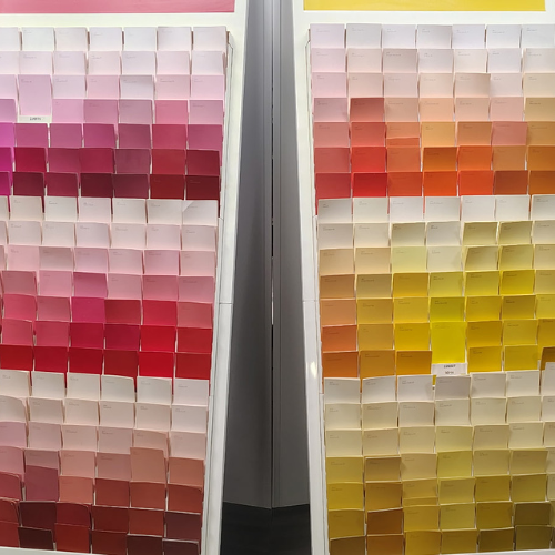 Two large paint-swatch displays show gradients from pale pink to deep red and from peach to vivid yellow, creating a colorful showroom scene.